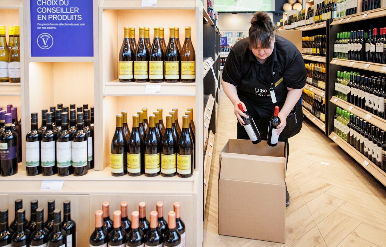 default-372 A woman puts wine bottles into a carboard box while standing in a store with bottles on every shelf.