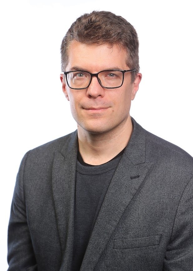 default-185 A portrait of a man wearing glasses dressed in dark-grey suits.